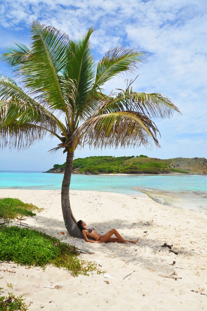 Girl under palm tree on sandy spit in BVI